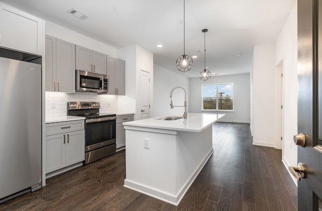 kitchen with appliances with stainless steel finishes, gray cabinetry, sink, a center island with sink, and dark hardwood / wood-style floors