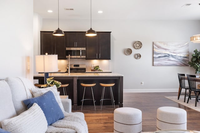 kitchen featuring a kitchen bar, appliances with stainless steel finishes, dark hardwood / wood-style flooring, tasteful backsplash, and hanging light fixtures