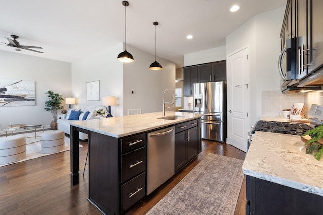 kitchen featuring a center island with sink, sink, appliances with stainless steel finishes, decorative light fixtures, and dark hardwood / wood-style flooring