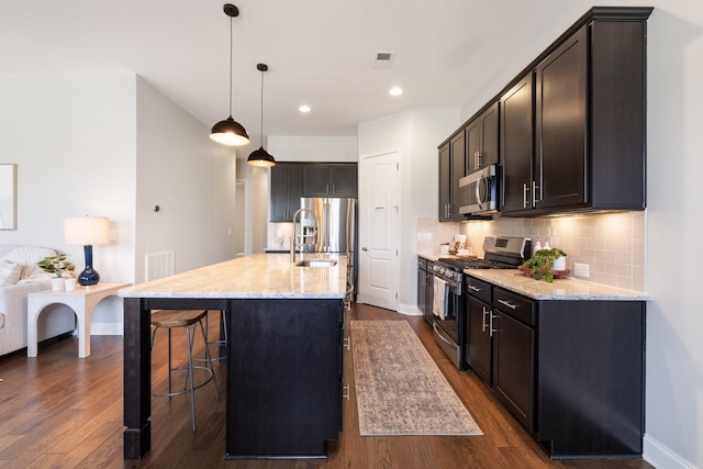 kitchen featuring dark wood-type flooring, sink, an island with sink, appliances with stainless steel finishes, and decorative light fixtures