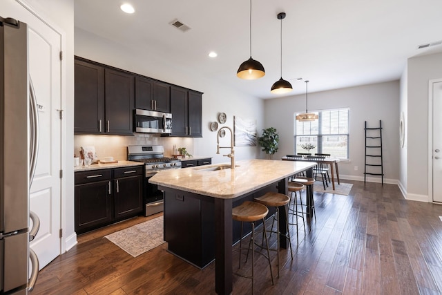 kitchen with a breakfast bar, sink, hanging light fixtures, an island with sink, and stainless steel appliances