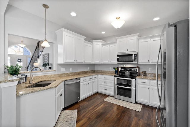 kitchen with appliances with stainless steel finishes, dark wood-type flooring, sink, white cabinets, and hanging light fixtures