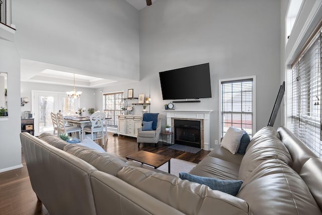 living room featuring a fireplace, a raised ceiling, dark wood-type flooring, and a high ceiling