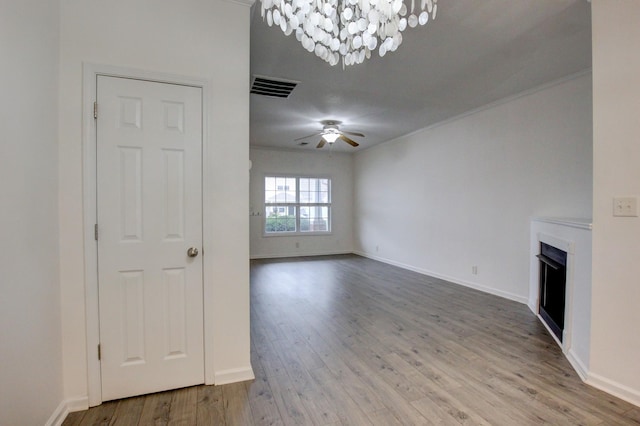 unfurnished living room featuring ceiling fan with notable chandelier, wood-type flooring, and ornamental molding