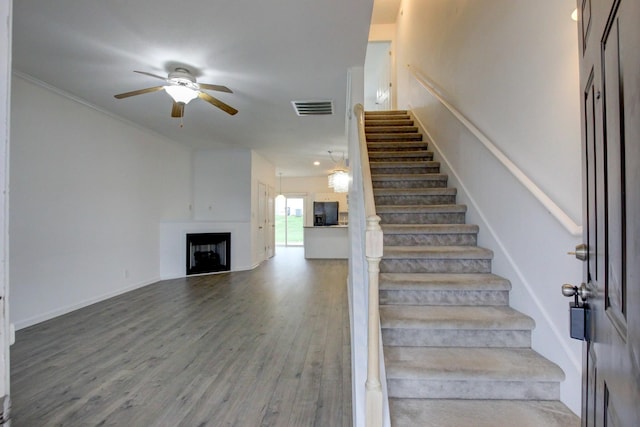 stairs with ceiling fan, crown molding, and wood-type flooring