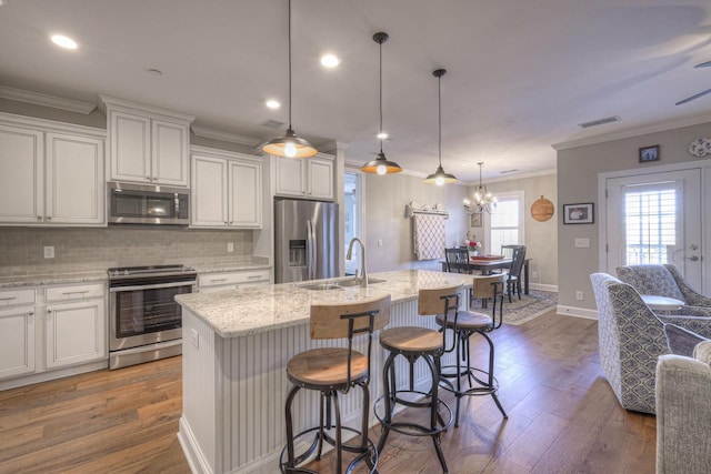 kitchen with decorative light fixtures, stainless steel appliances, a center island with sink, and sink