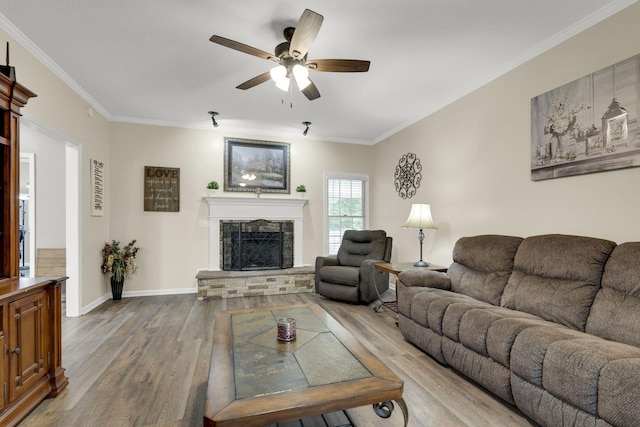 living room with ceiling fan, a stone fireplace, ornamental molding, and light hardwood / wood-style flooring