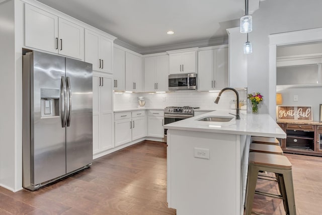 kitchen featuring white cabinetry, sink, decorative light fixtures, a breakfast bar, and appliances with stainless steel finishes