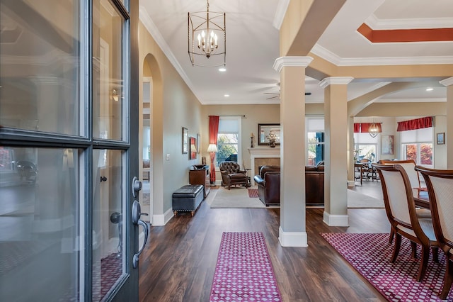 foyer featuring ornate columns, dark wood-type flooring, ceiling fan with notable chandelier, and ornamental molding