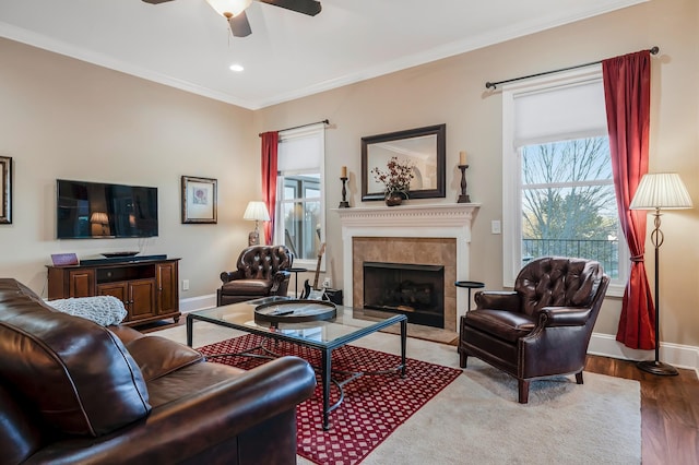 living room with a tile fireplace, hardwood / wood-style flooring, ceiling fan, and ornamental molding