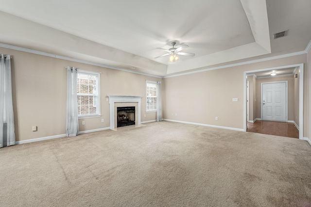 unfurnished living room with ceiling fan, a raised ceiling, crown molding, light carpet, and a fireplace