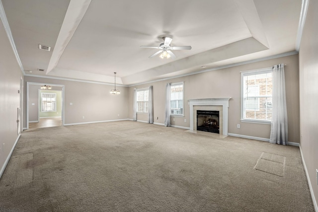 unfurnished living room featuring light carpet, ceiling fan with notable chandelier, crown molding, a fireplace, and a tray ceiling