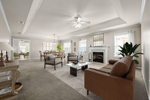 carpeted living room with a raised ceiling, ceiling fan with notable chandelier, and ornamental molding