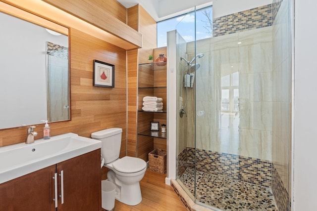 bathroom with walk in shower, vanity, wooden walls, hardwood / wood-style floors, and toilet