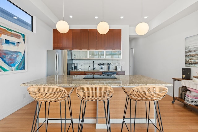 kitchen featuring decorative backsplash, stainless steel fridge, light hardwood / wood-style floors, and a breakfast bar area