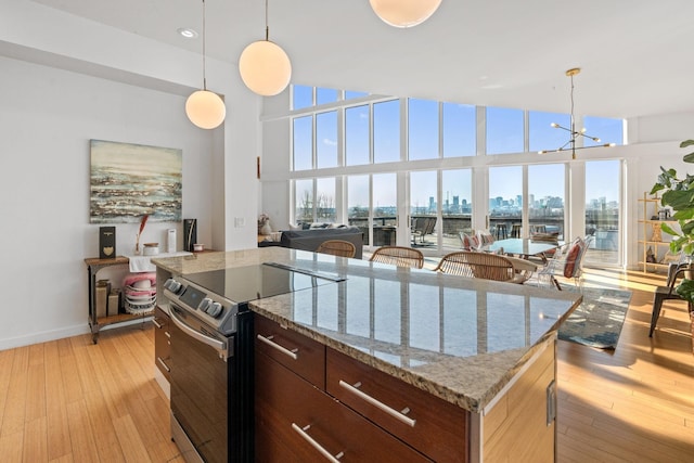 kitchen featuring stainless steel electric stove, a healthy amount of sunlight, light wood-type flooring, and a towering ceiling