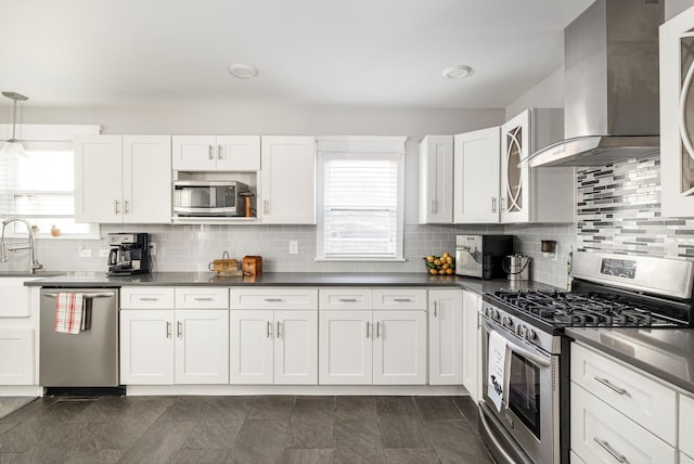 kitchen featuring white cabinets, wall chimney range hood, hanging light fixtures, tasteful backsplash, and stainless steel appliances