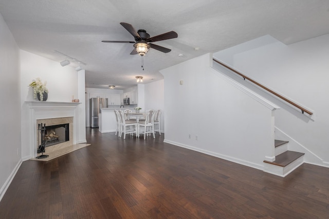 unfurnished living room featuring a textured ceiling, ceiling fan, dark wood-type flooring, and rail lighting