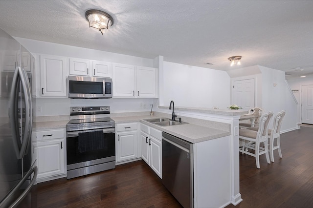 kitchen with kitchen peninsula, appliances with stainless steel finishes, sink, dark hardwood / wood-style floors, and white cabinetry