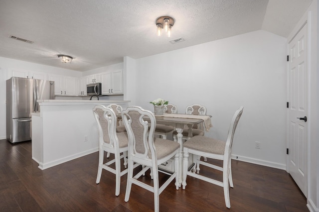 dining area featuring a textured ceiling, dark hardwood / wood-style floors, and vaulted ceiling