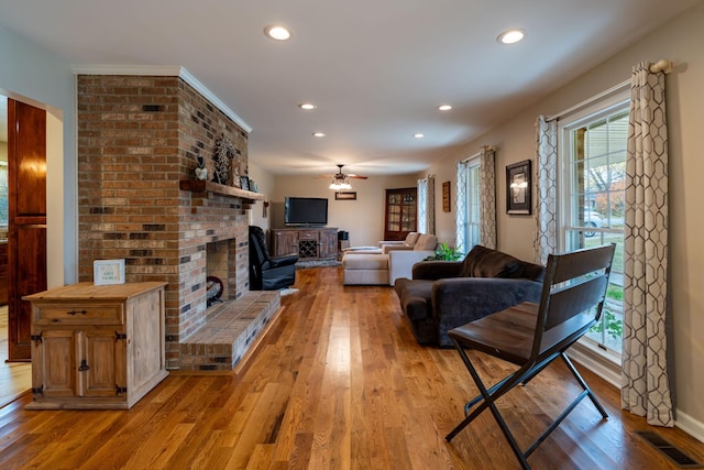 living room featuring ceiling fan, light wood-type flooring, and a fireplace