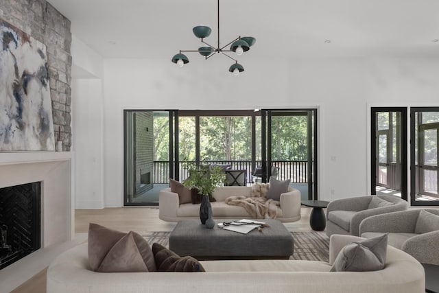 living room featuring a towering ceiling, light wood-type flooring, a large fireplace, and an inviting chandelier