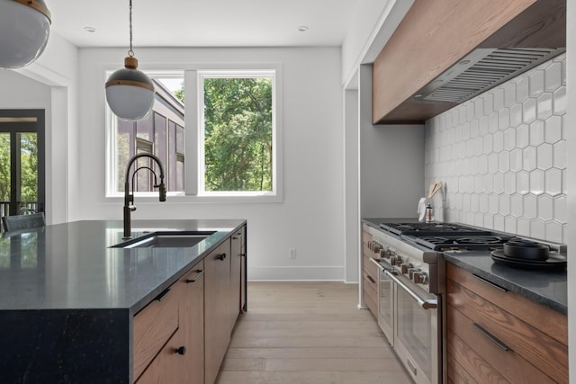 kitchen with decorative backsplash, light wood-type flooring, high end stove, sink, and decorative light fixtures