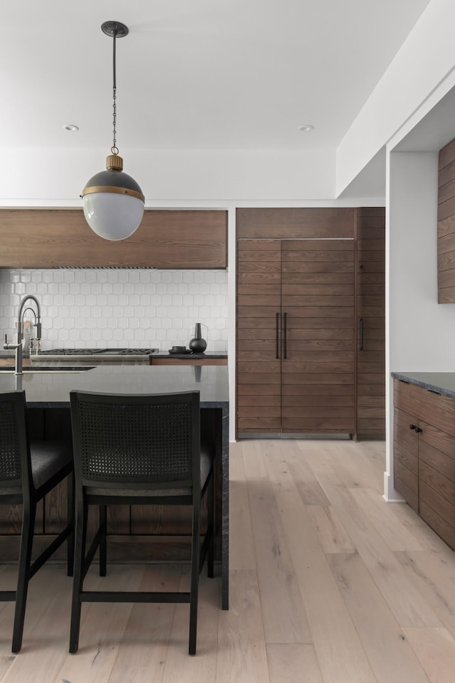 kitchen with a kitchen breakfast bar, light wood-type flooring, backsplash, and hanging light fixtures