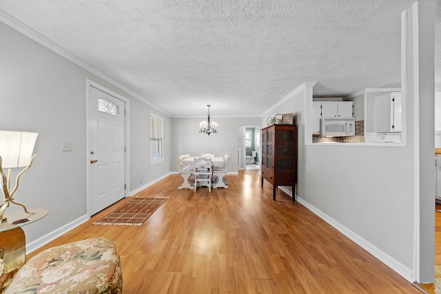 unfurnished dining area featuring a textured ceiling, a notable chandelier, light wood-type flooring, and ornamental molding