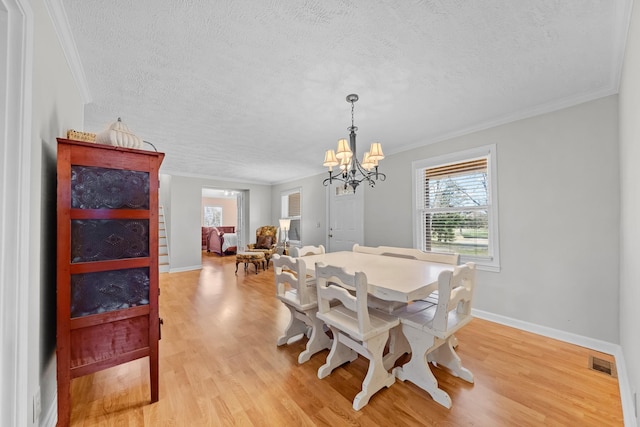 dining area featuring a textured ceiling, light hardwood / wood-style floors, an inviting chandelier, and ornamental molding