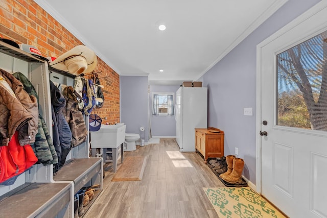 mudroom with light wood-type flooring, ornamental molding, and brick wall