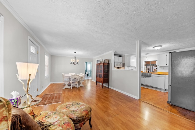 living room featuring sink, light hardwood / wood-style flooring, a notable chandelier, a textured ceiling, and ornamental molding