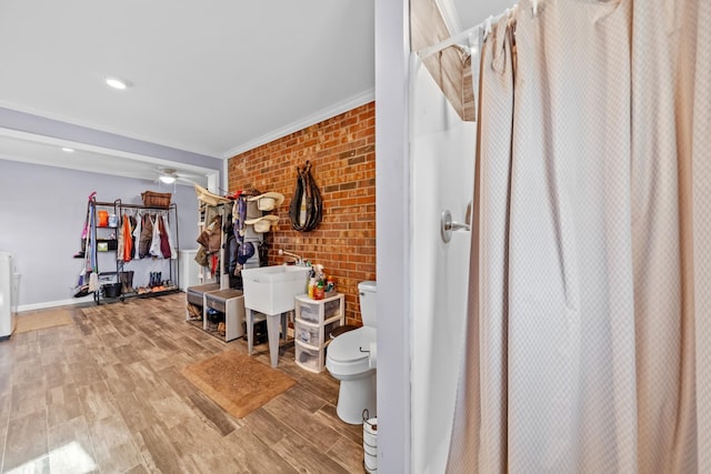 interior space with wood-type flooring, ceiling fan, crown molding, and brick wall