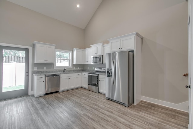 kitchen with high vaulted ceiling, appliances with stainless steel finishes, light hardwood / wood-style floors, light stone counters, and white cabinetry