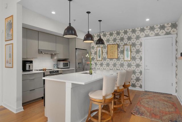 kitchen featuring gray cabinetry, a kitchen breakfast bar, sink, light wood-type flooring, and appliances with stainless steel finishes