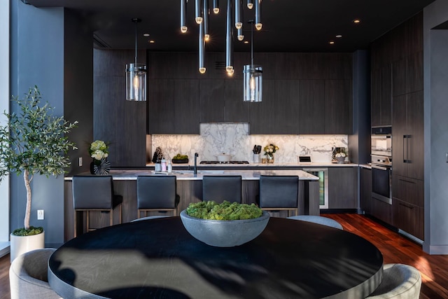 kitchen featuring backsplash, stainless steel oven, dark wood-type flooring, decorative light fixtures, and a center island