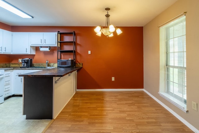 kitchen featuring white cabinets, light hardwood / wood-style flooring, a wealth of natural light, and hanging light fixtures