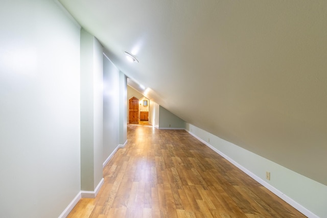 corridor with light hardwood / wood-style floors and lofted ceiling