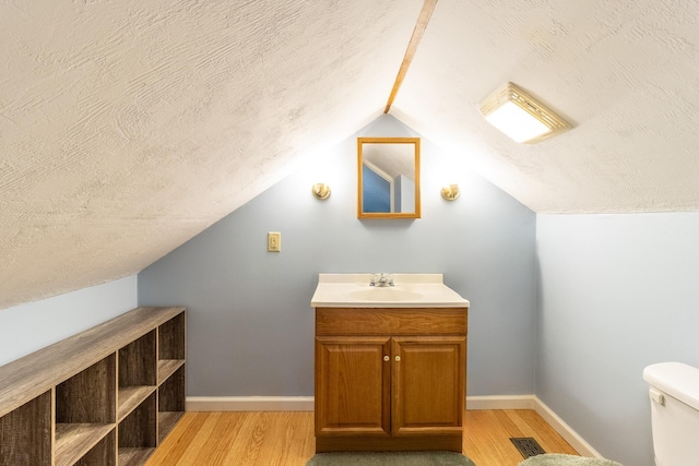 bathroom with vaulted ceiling, wood-type flooring, a textured ceiling, and toilet