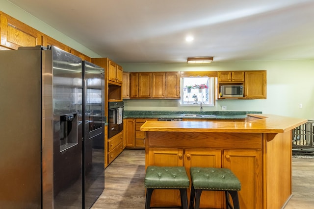 kitchen featuring butcher block countertops, wood-type flooring, a kitchen bar, a kitchen island, and appliances with stainless steel finishes