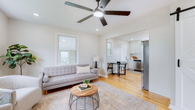 living room featuring ceiling fan, a barn door, and light hardwood / wood-style flooring