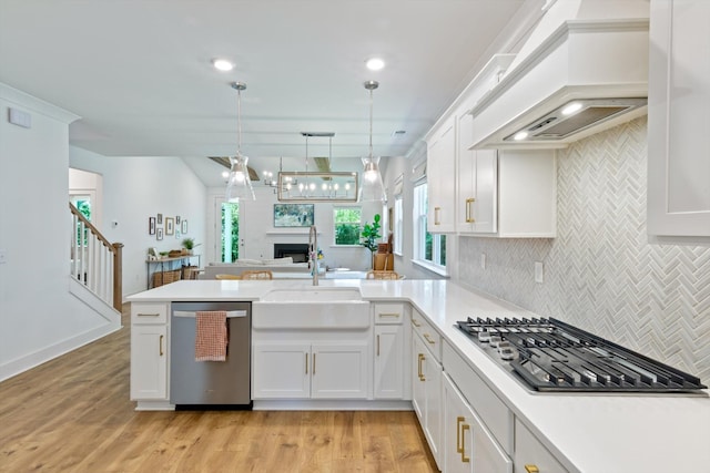 kitchen featuring kitchen peninsula, custom range hood, stainless steel appliances, light hardwood / wood-style floors, and hanging light fixtures