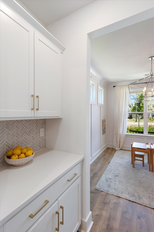 interior space with decorative backsplash, white cabinetry, hardwood / wood-style floors, and pendant lighting