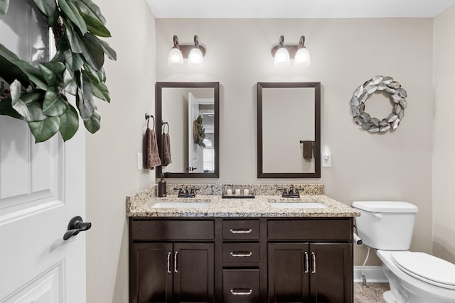 bathroom with baseboards, a sink, toilet, and double vanity