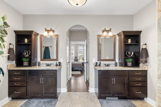 ensuite bathroom with baseboards, two vanities, and a sink