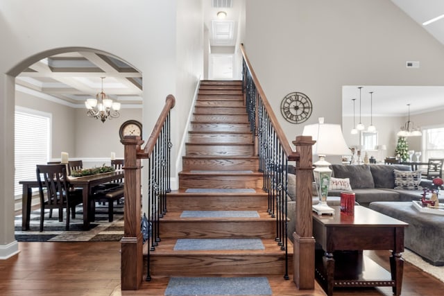 stairway with arched walkways, a towering ceiling, an inviting chandelier, and wood finished floors