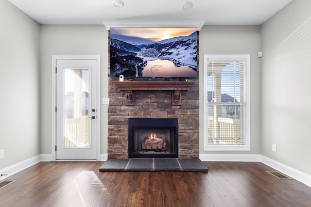 unfurnished living room with a stone fireplace, wood finished floors, visible vents, and baseboards