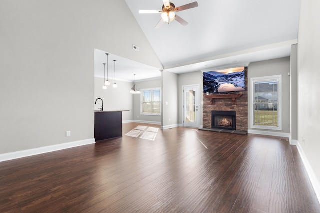 unfurnished living room with visible vents, dark wood-type flooring, a stone fireplace, baseboards, and ceiling fan with notable chandelier