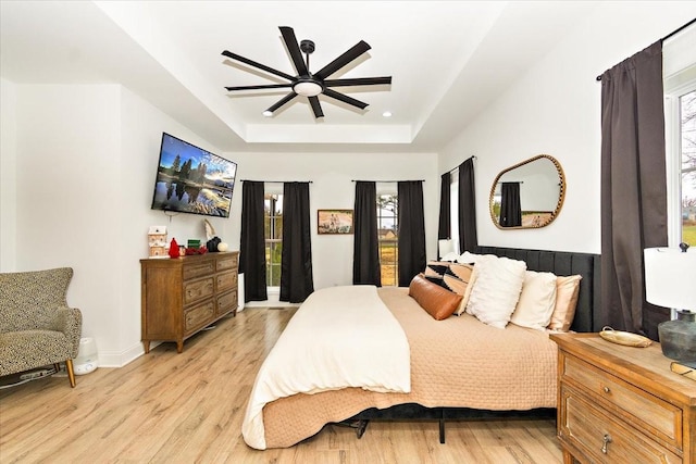 bedroom featuring ceiling fan, light hardwood / wood-style floors, a raised ceiling, and multiple windows