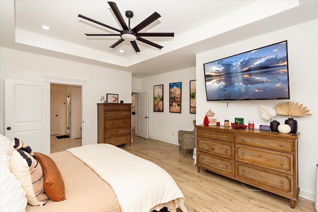 bedroom with a raised ceiling, ceiling fan, and light wood-type flooring